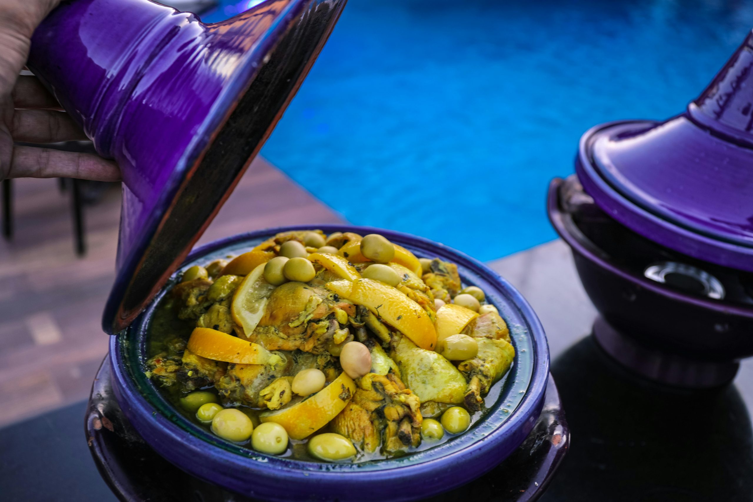 Delicious Moroccan tagine with olives and citrus in a purple pot by the poolside, evoking traditional cuisine.