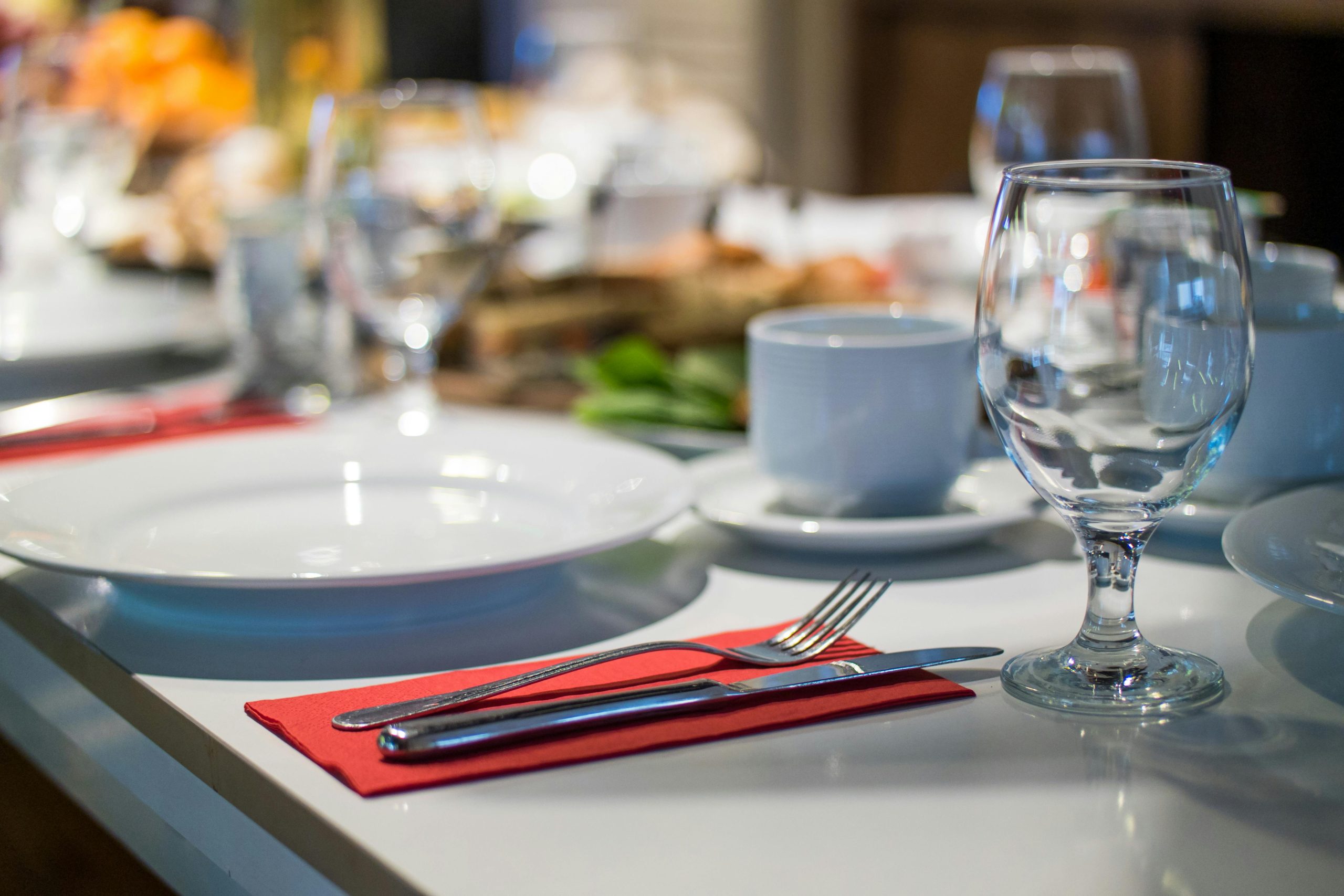 Close-up of an elegant dining table set with glassware, silverware, and red napkins in a restaurant setting.