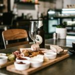 Rustic dining scene featuring craft beer, deli platter, and cappuccino in a cozy cafe atmosphere.