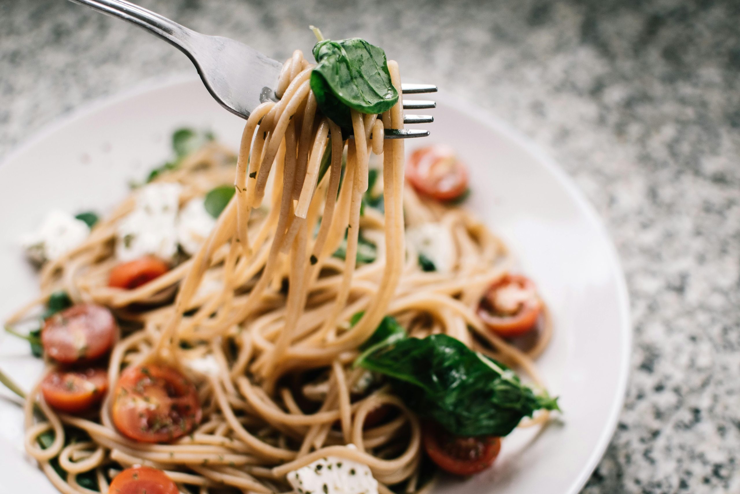 Delicious whole wheat pasta with fresh spinach, cherry tomatoes, and feta cheese in a close-up shot.