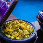 Delicious Moroccan tagine with olives and citrus in a purple pot by the poolside, evoking traditional cuisine.