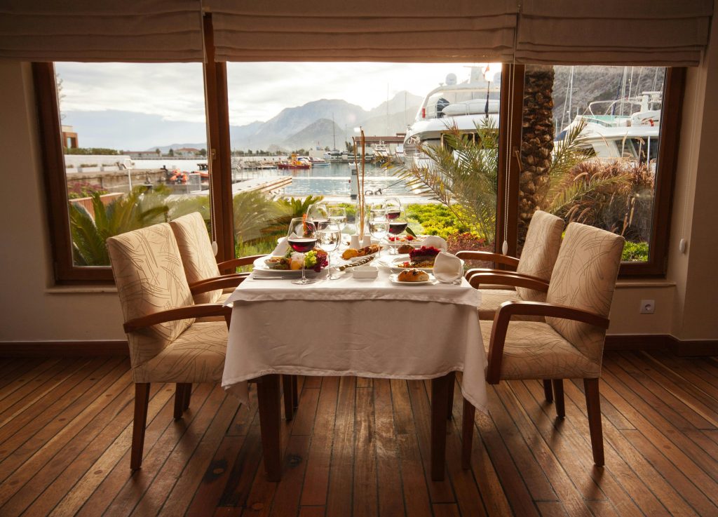 Elegantly set table in a seaside restaurant with a marina view, featuring gourmet dishes and fine dining setup.