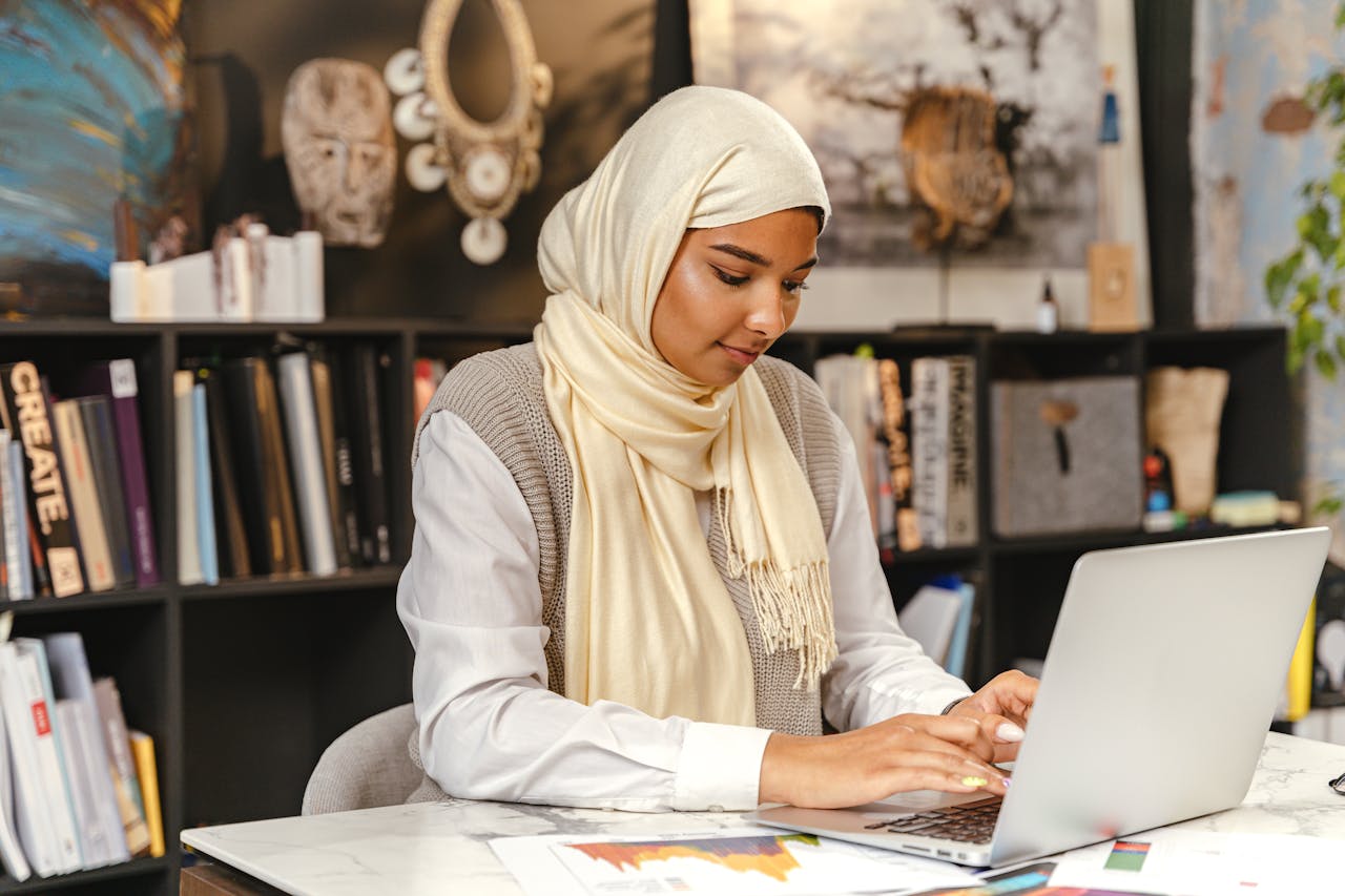 services-03 A Muslim woman in a hijab working on a laptop in a contemporary office setting, focused and professional.